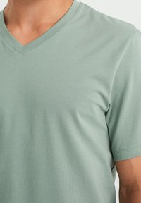 T-shirt vert clair en V fabriqué dans un tissu doux, à manches courtes, avec une texture lisse et un minimum de coutures au niveau du col.