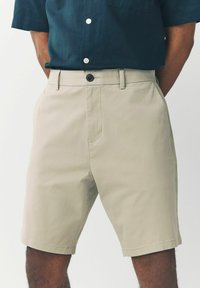Beige bomulds shorts med flad front, sidelommer og en enkelt knaplukning. Har en glat tekstur og skræddersyet pasform.
