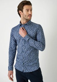 Blau gemustertes Langarmhemd mit Paisleymuster, Knopfverschluss und klassischem Kragen. Der Stoff wirkt glatt und hat eine strukturierte Passform.