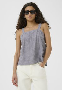 Szary lniany top na ramiączkach z szerokimi paskami i plisowanym detalem przy dekolcie, w połączeniu z białymi spodniami i czarnymi okularami w kocim kształcie.