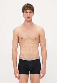 Melni bokseršortai ar pelēku jostu, uz kuras redzams "TOMMY HILFIGER" logo, izgatavoti no elastīga auduma komfortam un ciešai piegulšanai.