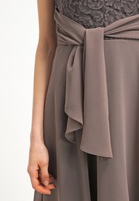 Robe grise avec un corsage en dentelle, une ceinture texturée à la taille, et une jupe fluide en tissu doux et léger.