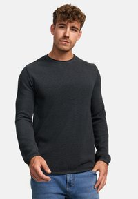 Pulover lung cu mânecă de culoare gri închis, având un gât rotund și un material texturat, asortat cu blugi albaștri. Model subtil vizibil pe tot parcursul.