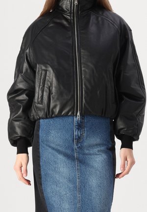 Černá zkrácená kožená bunda se zipem vpředu a kapsami, nošená přes dvoubarevnou modro-černou riflovou sukni.