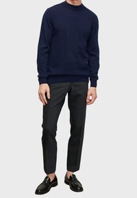 Marineblauwe gebreide sweater met textuurpatroon, met ronde hals, gecombineerd met antracietkleurige tapered broek en zwarte instappers.