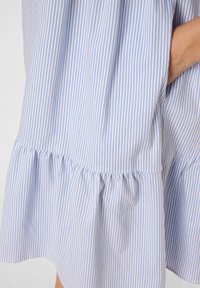 Blauw-wit gestreepte stoffen jurk, met een gelaagde ruches aan de onderkant, een lichte textuur en zijzakdetails.