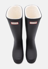 Black rubber knee-high boots with a white fleece lining and red-and-white "HUNTER" logo on the front. Smooth texture, wide opening.