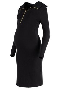 Schwarzes, geripptes Umstandskleid mit einem Reißverschlusskragen, langen Ärmeln und einer taillierten Silhouette, die einen wachsenden Bauch umschmeichelt.