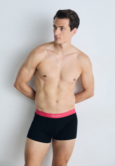 Schwarze Boxershorts mit einem pinken Bund, auf dem der Markenname "Paul Smith" in Weiß steht. Das Material wirkt glatt und formbeständig.