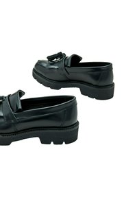 Zwarte leren loafers met een opvallende kwastdetail, voorzien van een dikke rubberen zool met een gestructureerde afwerking en een ronde vorm.