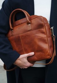 Brown leather bag with two top handles and a detachable shoulder strap, featuring a smooth texture and stitched accents.