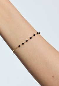 Złota bransoletka łańcuszkowa z czarnymi koralikami, charakteryzująca się delikatnym wzornictwem oraz cienkim, regulowanym zapięciem zapewniającym pewne dopasowanie do nadgarstka.