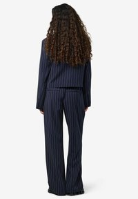 Marineblå pinstripet dress med cropped jakke og vide bukser. Stoffet har en jevn tekstur med knappedetaljer på ermene.