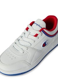 Sneaker bianca in pelle con accenti rossi e blu. Presenta una punta in rilievo, perforazioni, lacci e il logo Champion sul lato.