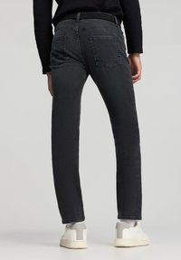 Jeans in denim nero con taglio dritto, cinque tasche e una finitura testurizzata sottile, abbinati a sneakers bianche.