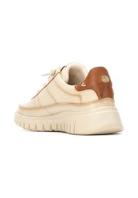 Zapatilla beige con cuero suave y un acento de cuero marrón en el talón. Suela de goma blanca gruesa con surcos texturizados.