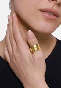 Anello in oro martellato indossato su un dito. L'anello presenta una banda ampia con una superficie texturizzata, che si abbina bene a una pelle liscia.