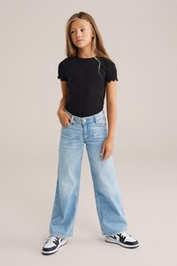 Melnā ribota īsām piedurknēm jaka ar viļņveida malām, apvienota ar gaiši zilajiem platajiem džinsiem un melnbaltām sporta kedām.