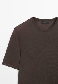 T-shirt en maille à manches courtes de couleur brun foncé avec col rond, montrant la section supérieure gauche et l'étiquette de la marque visible à l'intérieur du col.