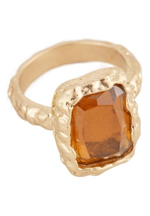 Gold ring with textured band holding a large, faceted amber gemstone in an irregular, rugged setting.