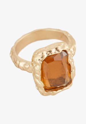 Gold ring with textured band holding a large, faceted amber gemstone in an irregular, rugged setting.