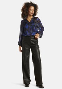 Sheer, long-sleeve blouse in blue with abstract patterns, paired with high-waisted black leather wide-leg trousers. Black ankle boots.