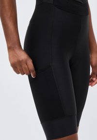 Εγγύς λήψη ενός ατόμου που φοράει μαύρα ποδηλατικά σορτς με δίχτυ πλαϊνή τσέπη, χέρι που ρυθμίζει την τσέπη στο μηρό.