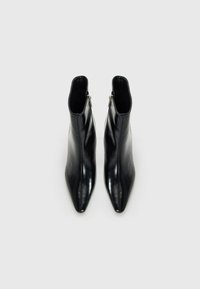 Une paire de bottines noires en cuir à bout pointu avec des zips latéraux, présentées de dessus sur un fond clair.