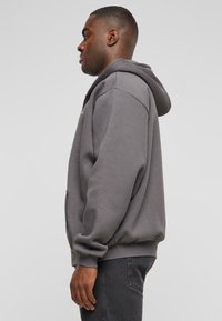 Grå hettegenser med frontglidelås, ribbestrikkede mansjetter og kant, laget av mykt fleece-materiale. Har to sidelommer.