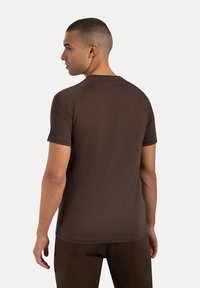 Camiseta marrón de manga corta con una textura suave, mangas raglán y un escote redondeado, vista desde la espalda.