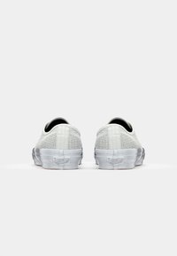 Witte canvas sneakers met een gestructureerde afwerking, zwarte voering en een rubberen zool. Heeft een laag profiel ontwerp en een logo detail aan de achterkant.