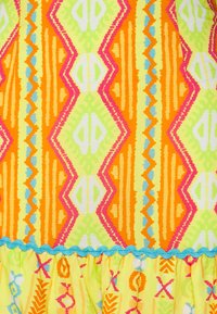 Tecido estampado colorido com designs em zig-zag e geométricos em amarelo-neon, laranja, rosa e verde, com um acabamento azul em forma de ondas.