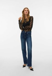 Svart blonder langermet topp med gjennomsiktige detaljer og pynt, kombinert med mørkeblå rette jeans og svarte spisse hæler.