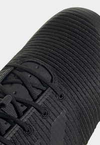 Gros plan de l'avant d'une basket noire avec un tissu côtelé texturé et des lacets noirs passant dans les œillets.