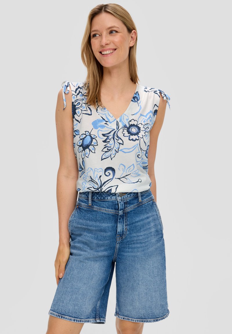 Mouwloze top met bloemenpatroon in wit en blauw, met strikdetails op de schouders, gecombineerd met knielange blauwe denim shorts.