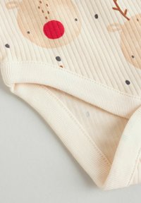 Ribbet spædbarn body i lys beige med rensdyrmønster, der har rød næse og mørke prikker, blød tekstur og elastiske cuffs for en tætsiddende pasform.