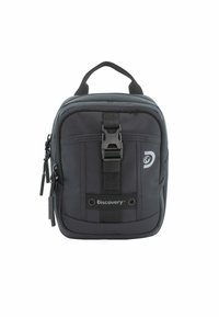 Mochila negra de tela con forma rectangular, que cuenta con un asa superior, cierre de cremallera, hebilla frontal y detalle del logo. Dos bolsillos con cremallera son visibles.