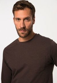 Langsleeve bruin shirt met een ronde halslijn, voorzien van een klein borstzakje en een gladde textuur. Eenvoudig, schoon ontwerp.