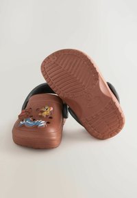 Sabots en plastique marron avec des sangles noires, ornés de personnages de dessins animés. Semelles texturées pour l'adhérence, plusieurs trous de ventilation sur toute la surface.