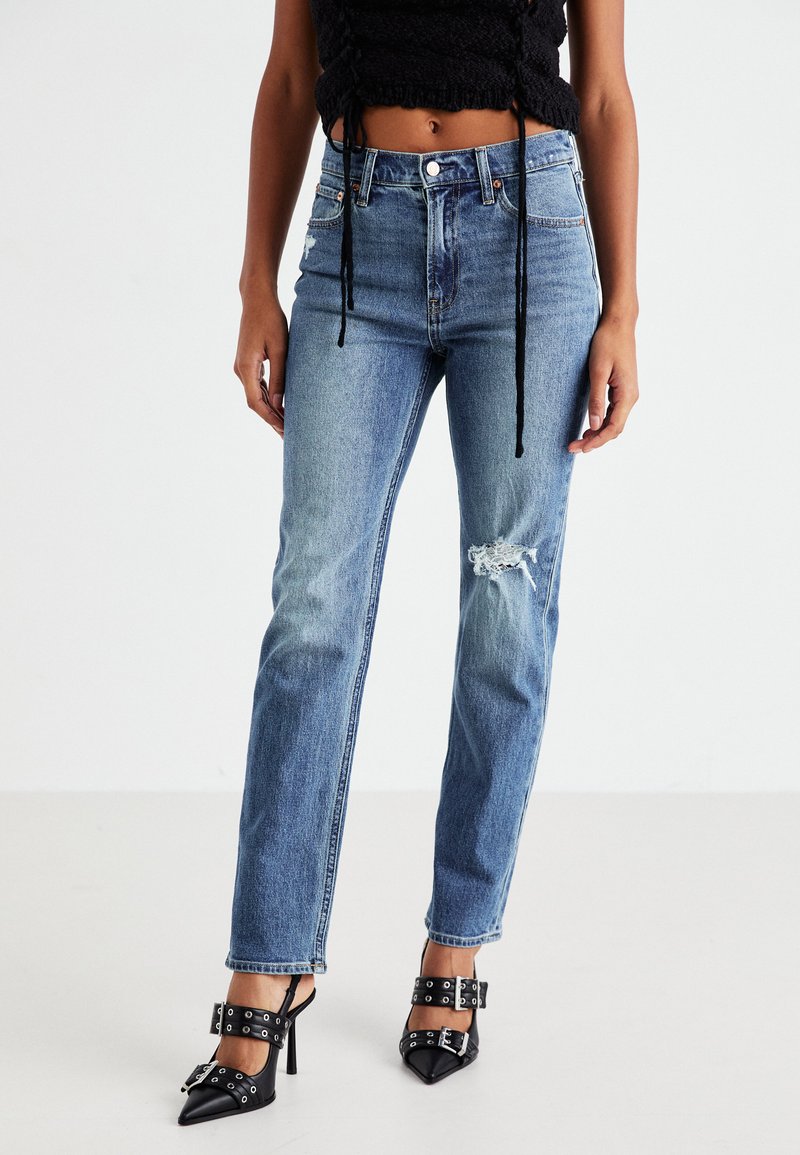 Light blue jeans with a high waist, straight legs, and a distressed knee detail. Worn with black heeled shoes accented with silver hardware.