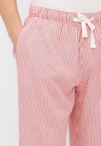 Punased ja valged triibulised lounge-püksid, millel on elastne vöökoht ja pael. Kude paistab pehme ning lõige on mugav, lisaks on küljetaskud.