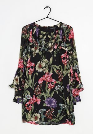Robe noire à manches longues florale avec des volants sur la poitrine et les manches, présentant des motifs de fleurs roses, violettes, blanches et vertes, accrochée à un cintre noir.