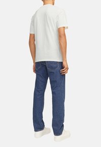 T-shirt en coton gris clair à manches courtes, associé à un jean en denim bleu. Des baskets blanches complètent la tenue, mettant en valeur un style décontracté.