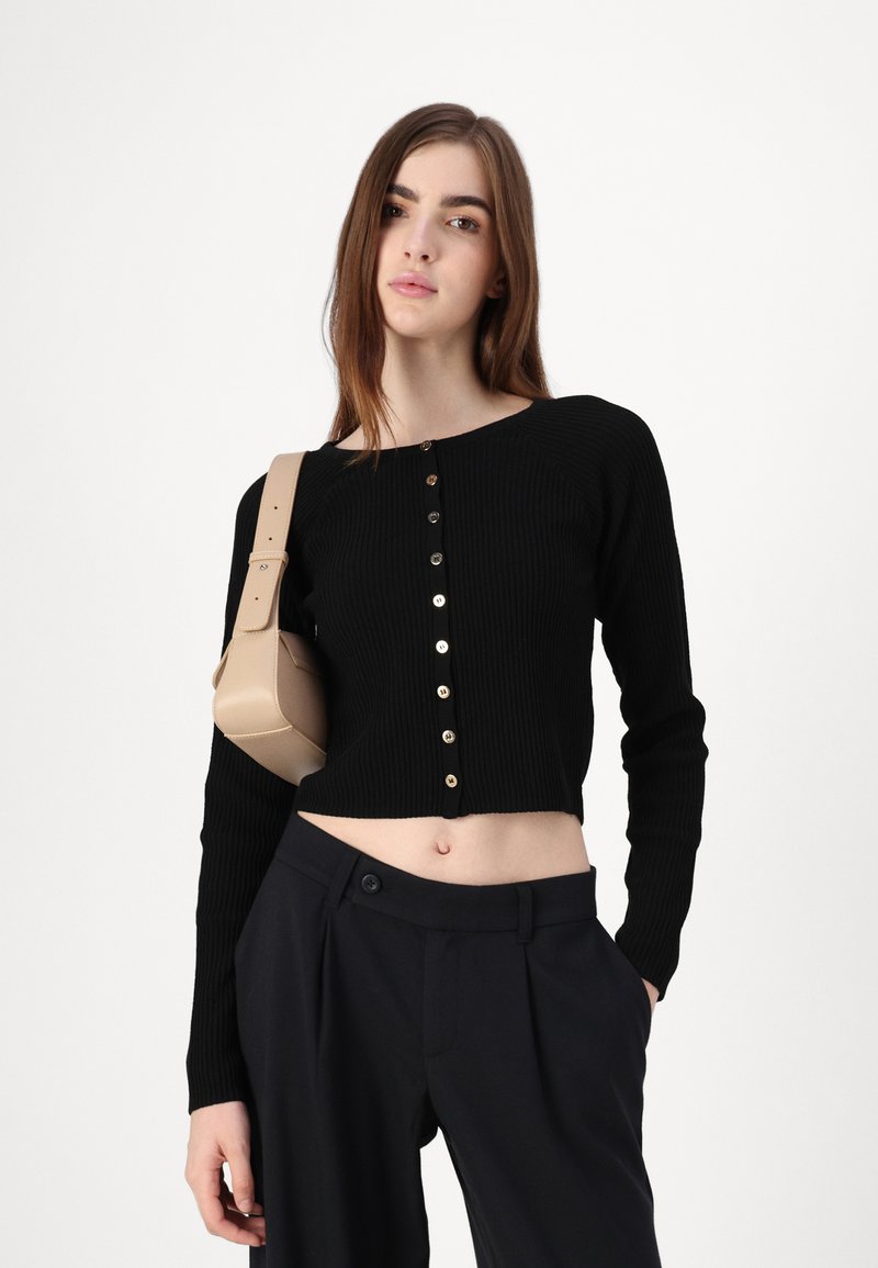 Suéter corto de punto acanalado negro con cuello redondo y botones dorados en el frente, combinado con pantalones de cintura alta en color marino.