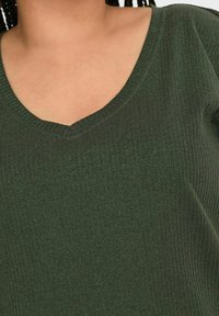 Mørkegrøn strikket top med V-hals, der har ribbet tekstur og en subtil glans i stoffet.