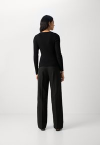 Haut noir à manches longues côtelé avec un décolleté arrondi, associé à un pantalon noir ample ; texture lisse et design ajusté.