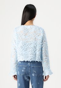 Light blue cropped sweater with textured, frayed detail and long sleeves; worn over patterned denim jeans. Transparent fabric layers visible.