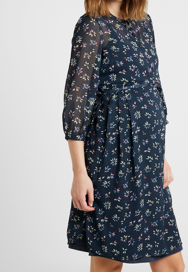 Robe florale marine à manches longues transparentes, avec une taille ceinturée et des motifs de fleurs colorées éparpillés sur l'ensemble.