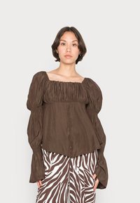 Blusa castanha de mangas longas pregueada com decote quadrado. O tecido é suave e as mangas são volumosas, combinando com calças com padrão de zebra branco e castanho.