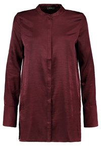 Burgunderry sident skjorta med knappar och mandarin-krage, långa ärmar och rak skärning. Har sidoflikar för rörelse.